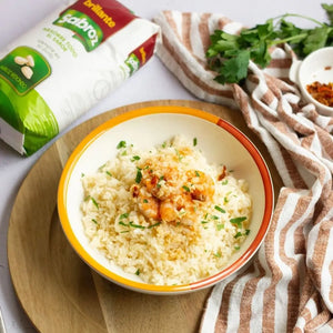 A bowl of white rice with shrimp and herbs, with a Sabroz rice package displayed nearby